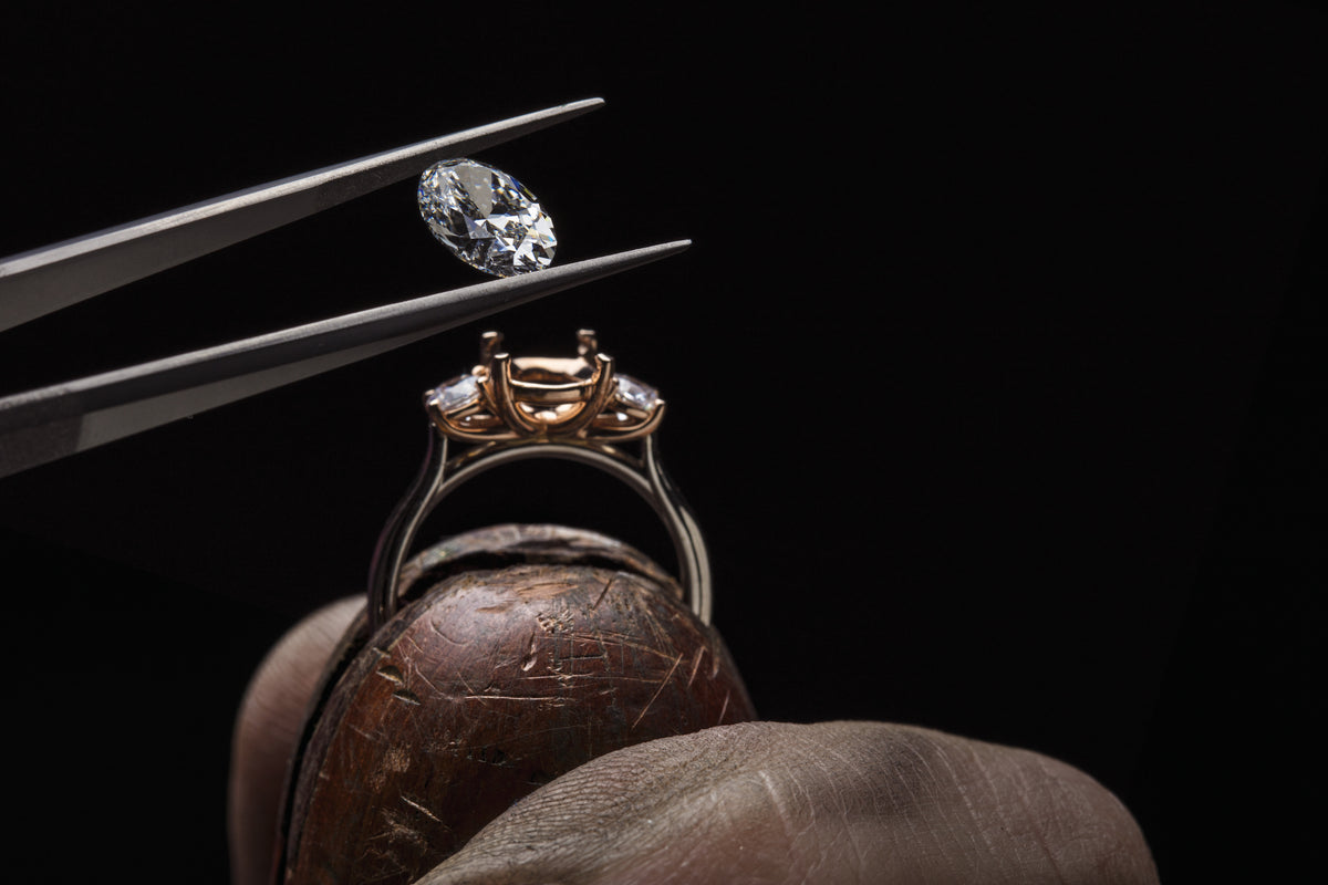 A custom jeweler holding the bespoke ring and placing the lab-grown diamond into the ring with jewelry tweezers