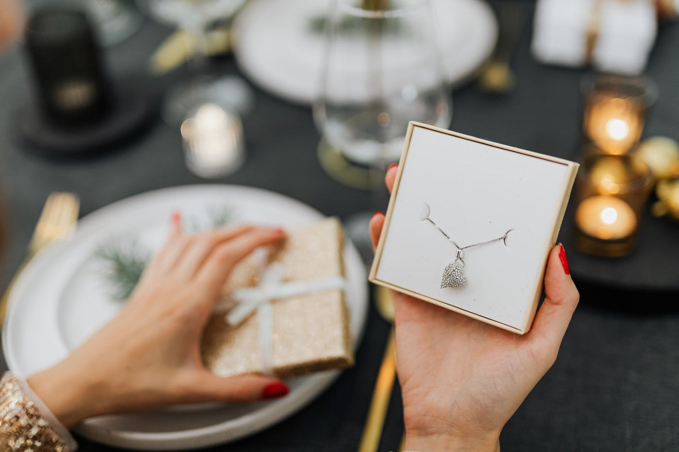 Woman at a dining table with fancy settings, opening a holiday jewelry gift for her