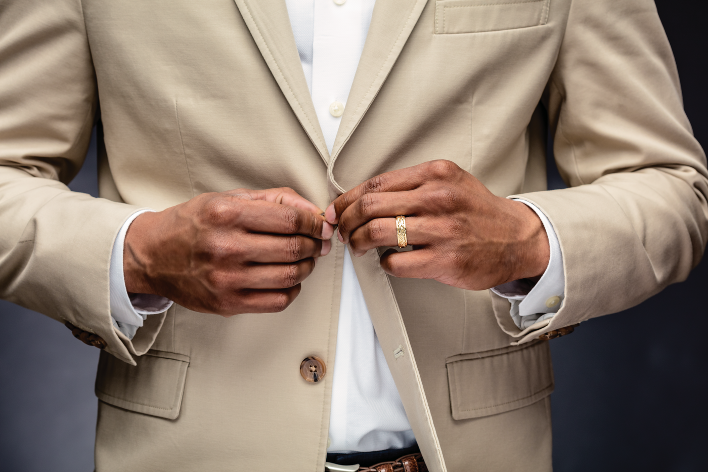 Well-dressed man in a brown suit buttoning up his jacket and showing his luxury and sustainable wedding band.