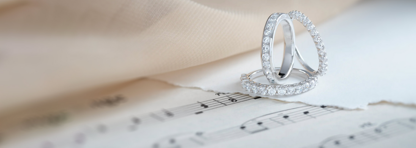 Three gorgeous eternity bands with lab-grown diamonds on top of papers with music notes on them.