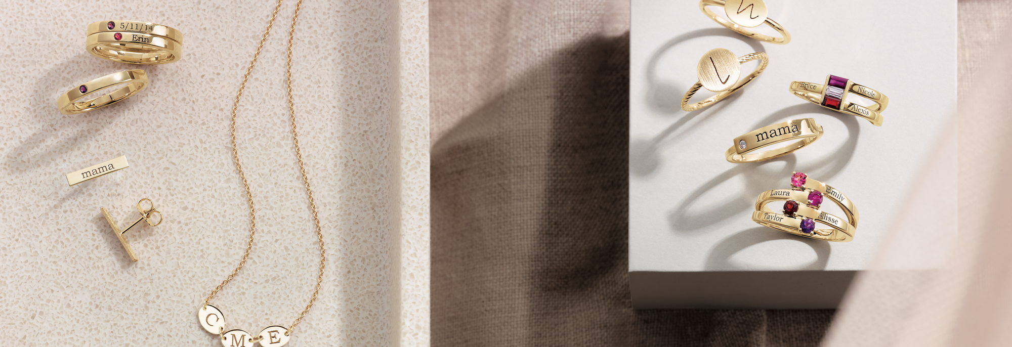 White square box on top of beige fabric displaying gold rings with engraved initials, a gold ring engraved with "mama" and pink and purple lab-grown diamonds on gold rings.