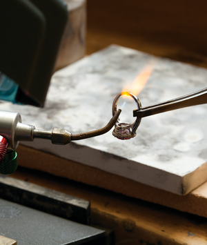 Torch and jewelry tweezers being used to custom-make a ring and seal the band after sizing.