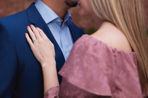 A couple dressed in a blue suit and pink dress, where she has her hand on his chest showing off her custom-made lab-grown diamond.