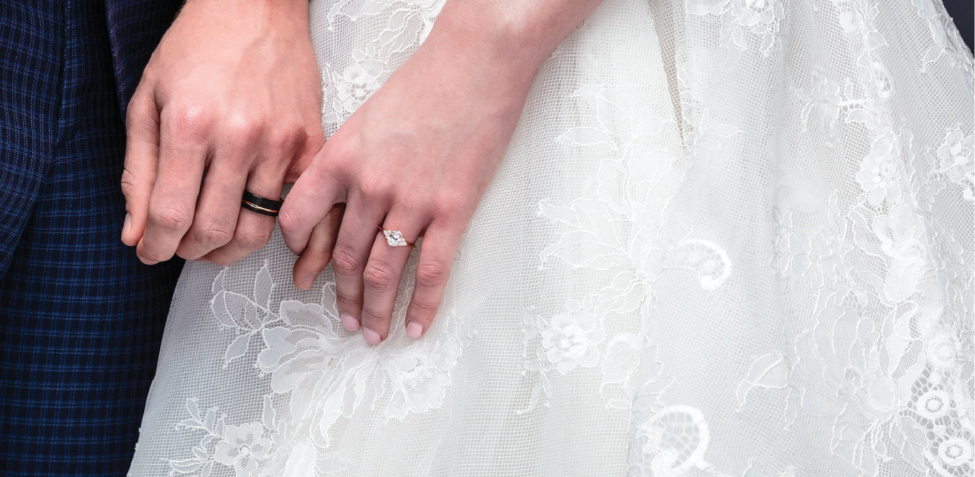 A bride and grooms hands holding each other showing off their wedding bands, and her Carbon Diamond engagement ring.